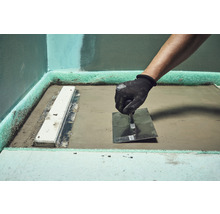 Handwerker bearbeitet Estrich mit einer Glättkelle in einem Badezimmer