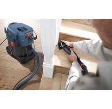 Eine Person verwendet einen Multifunktionsschleifer zum Schleifen einer Holztreppe, wobei ein Staubsauger für eine saubere Arbeitsumgebung sorgt.