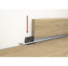 Illustration der Montage einer Holzfußleiste mit Kabelkanal und rotem Pfeil, der die Richtung der Montage anzeigt.