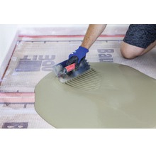 Fliesenleger trägt Fliesenkleber auf Entkopplungsmatte auf