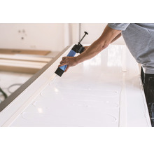 Handwerker trägt mit einer Kartuschenpistole Kleber auf eine weiße Oberfläche auf.