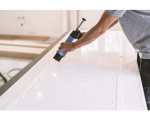 Handwerker trägt mit einer Kartuschenpistole Kleber auf eine weiße Oberfläche auf.