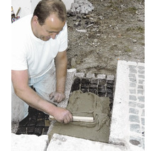 Handwerker verfugt Pflastersteine mit Zementmörtel