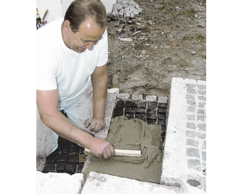 Handwerker verfugt Pflastersteine mit Zementmörtel