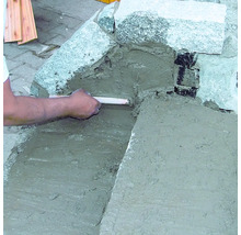 Eine Person verfugt Steine mit Mörtel.