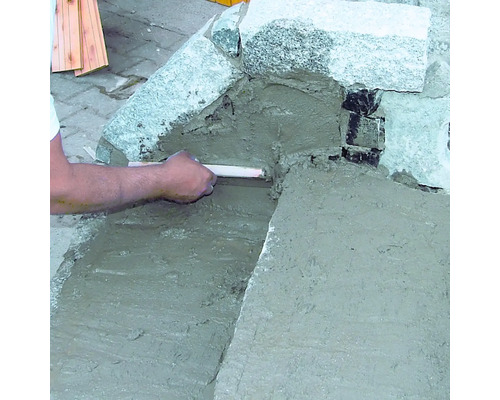 Eine Person verfugt Steine mit Mörtel.