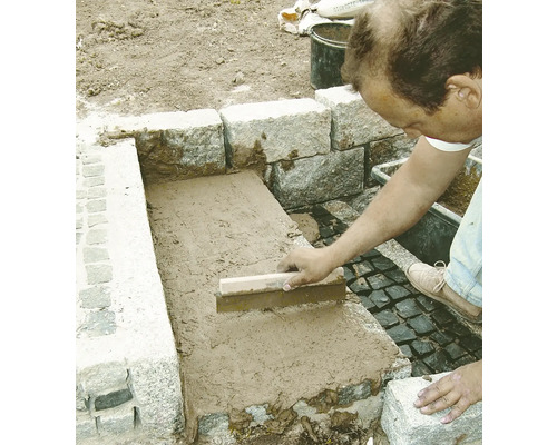 Handwerker verfugt Steine mit einem Fugenbrett im Außenbereich.