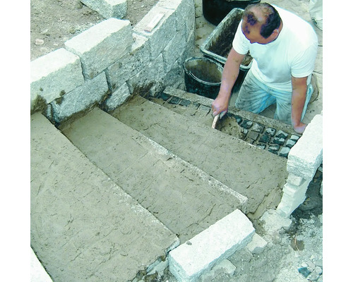 Handwerker verlegt Pflastersteine auf einer Steintreppe im Außenbereich.