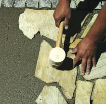 Eine Person verlegt Natursteine mit einem Gummihammer.