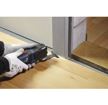 Eine Person benutzt ein Multifunktionswerkzeug zum Schneiden eines Holzbodens an einer Tür.