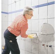 Mann spachtelt eine Wand im Badezimmer mit Fliesenkleber.