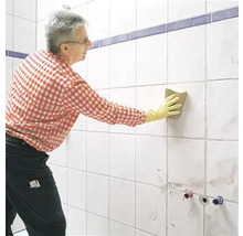 Mann reinigt Fliesen mit einem Schwamm im Badezimmer.