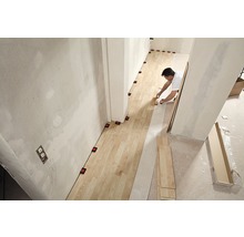 Ein Mann verlegt Holzfußboden in einem Raum mit Nivellierhilfen.