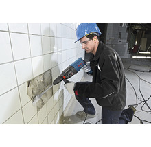 Mann mit Schutzhelm und Schutzbrille benutzt Bohrhammer an gefliester Wand