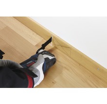 Eine Person benutzt einen Multifunktionsschneider an einer Holzfußleiste, um einen präzisen Schnitt durchzuführen.