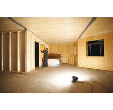 Innenansicht eines Raumes im Rohbau mit einer Person, die Dämmmaterial anbringt