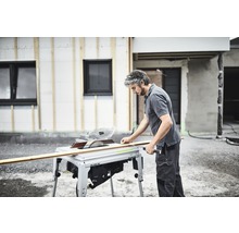 Handwerker beim Zuschnitt eines Holzbretts mit einer Tischkreissäge vor einem Haus im Bau