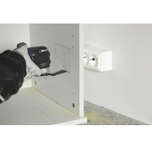 Eine Person verwendet ein Multifunktionswerkzeug, um einen Ausschnitt in ein Holzstück zu schneiden, in der Nähe einer Steckdose.