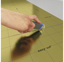 Hand schneidet Dämmunterlage mit einem Cuttermesser.