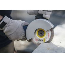 Eine Person schneidet mit einer Flex und Schutzhandschuhen Stein.