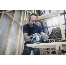 Ein Mann sägt ein Holzbrett mit einer Bosch Tauchsäge in einer hellen Werkstatt.