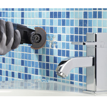 Ein Arbeiter mit Handschuhen entfernt Fliesen mit einem Multifunktionswerkzeug in einem Badezimmer