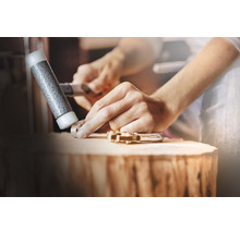 Mann formt ein Werkstück mit einem Hammer auf einem Holzblock.