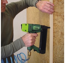 Eine Person befestigt eine Holzleiste mit einem Druckluftnagler an einer Holzwand.