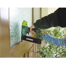 Eine Person befestigt mit einem Druckluftnagler eine Leiste an einem Fensterrahmen.