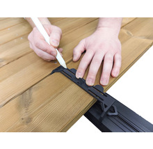 Eine Person zeichnet mit einem Stift auf eine Holzterrasse mit einer schwarzen Abstandshalterung.