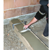 Eine Person glättet Beton in einer Holzform mit einer Glättkelle.