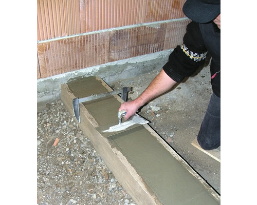 Eine Person glättet Beton in einer Holzform mit einer Glättkelle.