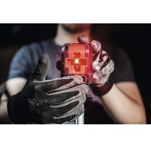 Eine Person hält einen Baulaser mit roten Laserstrahlen in der Hand.