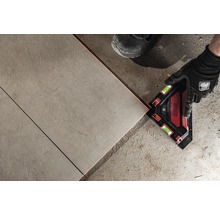 Ein Mann verlegt Fliesen mit einem Laser-Winkelmesser.