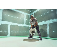 Mann gießt Ausgleichsmasse auf einen Boden in einem Raum mit vorbereiteten Wänden