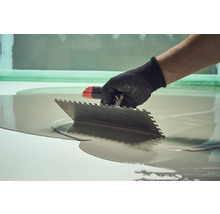 Handwerker verteilt Bodenausgleichsmasse mit einer Glättkelle