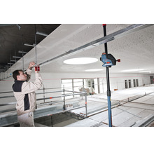 Ein Mann montiert eine Deckenkonstruktion mit einem Kreuzlinienlaser und einem Deckenstativ in einem Raum.