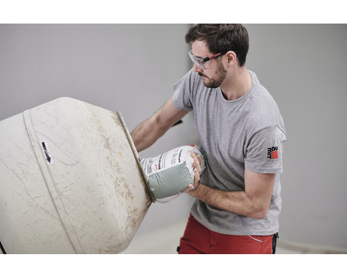 Mann mit Schutzbrille gießt 30 kg Sack Mörtel in einen Betonmischer