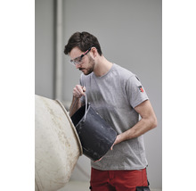 Mann mit Schutzbrille schüttet Inhalt aus einem Eimer in einen Betonmischer