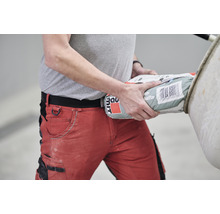 Mann mit roter Arbeitshose trägt einen Sack Baumaterial.