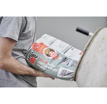 Person trägt Sack mit Fertigbeton für Garten- und Landschaftsbau