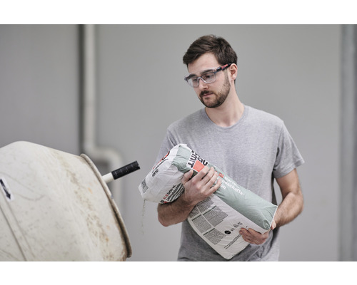 Mann schüttet Estrichmörtel in einen Betonmischer.