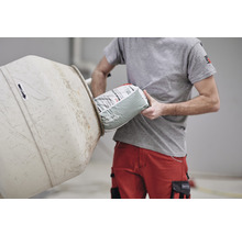 Mann schüttet eine Sack Zement in einen Betonmischer