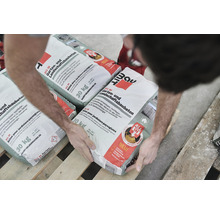 Person hantiert mit Säcken Baumit All in Garten- und Landschaftsbaubeton 30 Kilogramm auf einer Palette