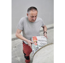 Ein Mann leert einen Sack Betonmischung in einen Mischer.