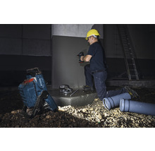 Handwerker bei der Arbeit mit Bohrmaschine, Baustrahler und Abwasserrohren auf einer Baustelle