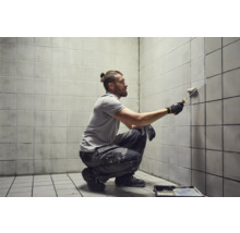 Mann streicht Fliesenwand mit Farbroller