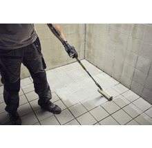 Handwerker streicht Fliesenboden mit Farbroller in einem Badezimmer.