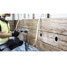 Ein Handwerker bohrt mit einer Akku-Bohrmaschine ein Loch in eine Wand mit Holzstruktur.
