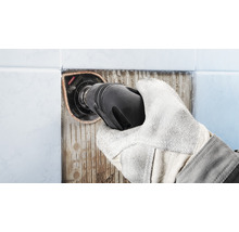 Hand mit Schutzhandschuh entfernt Fliesen mit einem Multitool